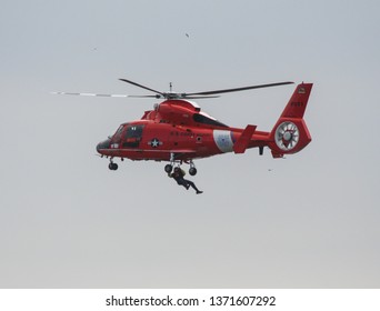 Los Angeles, CA / USA - February 14, 2006: A Bright Red US Coast Guard Dolphin Helicopter Conducts Training Rescue Operations Off Point Vicente As A Person Dangles From A Wince In The Air Beneath.