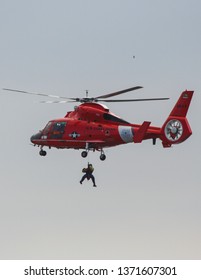 Los Angeles, CA / USA - February 14, 2006: A Bright Red US Coast Guard Dolphin Helicopter Conducts Training Rescue Operations Off Point Vicente California, A Person Dangling Beneath  On A Winch.