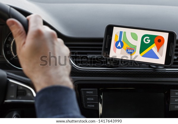 LOS ANGELES, CALIFORNIA -\
JUNE 6, 2019: Close up to male driving and using different\
navigation application Google maps, Apple Maps. An illustrative\
editorial image