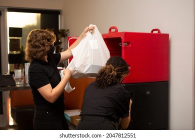 Los Angeles, California, United States - 08-24-2021: A View Of Two Female Employees Managing To-go Food Orders Going In And Out Of A Food Locker, Seen At A Local Restaurant.