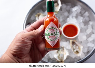 Los Angeles, California, United States - 10-02-2021: A Top Down View Of A Hand Holding A Bottle Of Tabasco Hot Sauce Over A Tray Of Raw Oysters.