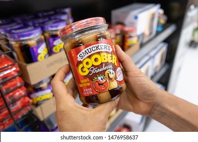 Los Angeles, CA/USA 08/09/2019 Shoppers Hand Holding A Jar Of Smucker's Goober Brand Peanut Butter And Strawberry Jelly Stripes In A Supermarket Aisle