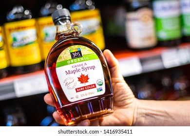 Los Angeles, CA/USA 6/1/2019  Shoppers Hand Holding A Plastic Bear Jar Of 365 Whole Foods Brand Of Organic Grade A Maple Syrup On A Supermarket Aisle
