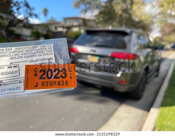 LOS ANGELES, December 28th, 2021:\
California Car registration tags for 2023 close up, held next to a\
parked car in a residential\
neighborhood.