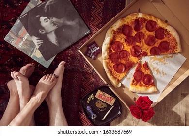LOS ANGELES, UNITED STATES - Feb 09, 2018: A couple's feet on the floor tangled together in a romantic embrace with records, Kiva weed Chocolates, Raw rolling paper, weed, joint, pipe and pizza