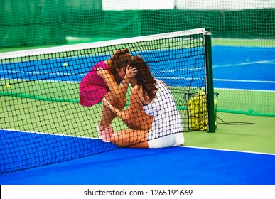 Lose Again. Frustrated Sexy Young Woman In Sports Clothing Sitting Near A Tennis Net. A Workshop Colleague Comforting Her Rival Losing Match. The Sportswoman Is Upset