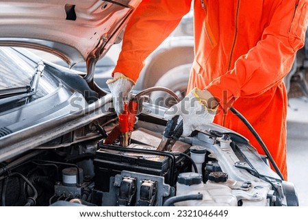 lose-up of a mechanic using a jumper cable to start a car battery when experiencing a dead battery. in the service center Concept of pre-departure and lifetime inspection and maintenance services