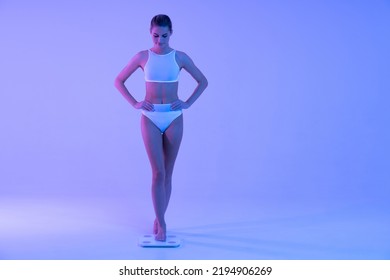 Losing Weight, Dieting, Flat Stomach, Fitness Training. Full Length Neon Portrait Of Slender Woman Stepping On Weight Scales To Check Fat Loss After Intensive Workout