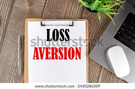 LOSS AVERSION text on a paper clipboard with laptop and mouse on wooden background , business concept