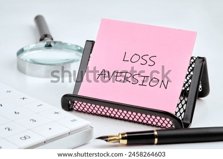 LOSS AVERSION text written on a pink sticker on a black stand on a white background