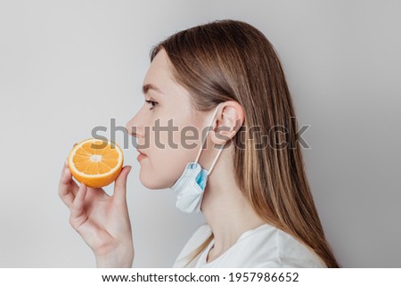 Loss of smell concept. Caucasian young woman in a medical mask sniffing an orange on a white background in the studio. profile view