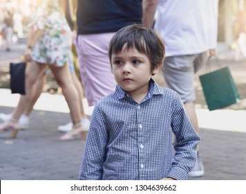 Lost Child Boy Standing On A Busy Crowded Street In Big City,Little Boy Looking Around Finding Parent With Worrying Face On Blurry Background Of People Walking On Street