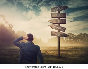 Lost and confused businessman in front of a signpost showing impossible directions. Business dilemma and difficult choice concept. Choosing the correct way on the road sign