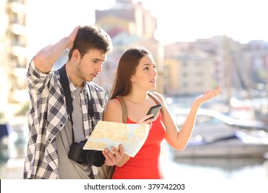 Lost couple of tourists searching location in a guide and smart phone with a port in the background - Shutterstock ID 379742203