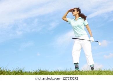 Lost Female Golfer Holding Golf Club Looking For Golf Ball Against Clear Blue Sky. Wearing Sunglasses.