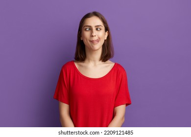 I lost my mind. Pretty brunette girl in red t-shirt demonstrating tongue and making stupid face with crossed eyes. Looks as a crazy woman showing ridiculous grimace. Posing over purple background - Shutterstock ID 2209121485