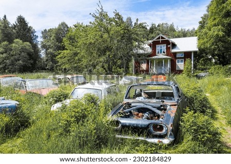Lost place with forgotten wooden house and classic car wrecks around overgrown with plants