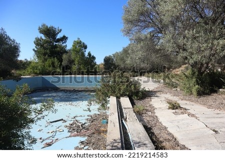 Lost places: views of an empty pool from a not abandoned hotel complex in Izmir, Turkey. The swimming area is left to decay and already overgrown by nature. Forgotten ruins in a vacation paradise.