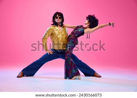 Lost in Rhythm. Young couple, man and woman in bright retro costumes in dance pose against gradient pink studio background. Concept of American culture, 70s, 80s fashion, music, comparisons of eras.