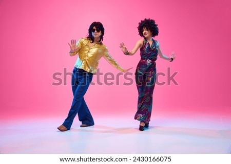 Lost in Rhythm. Young couple, man and woman in bright retro costumes in dance pose against gradient pink studio background. Concept of American culture, 70s, 80s fashion, music, comparisons of eras.