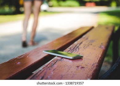 Lost Smartphone On Bench In Public Park. Woman Leaving From Bench Where She Forget Her Smart Phone. 