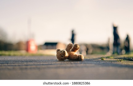 Lost Teddy Bear With Sad Face Lying On Footpath With Blurry People ,Lonely Bear Doll Laying Down On The Brick Floor In Gloomy Day, Lost Toy Or Loneliness Concept, International Missing Children