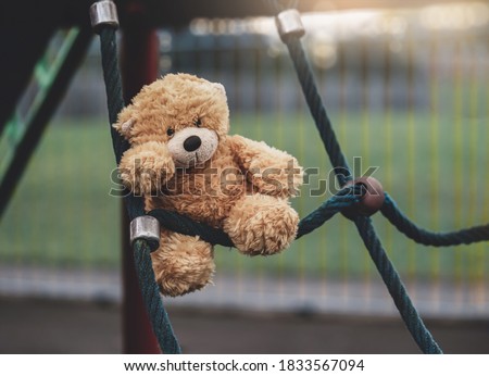 Lost teddy bear toy lying on rope frame at playground in gloomy day, Lonely and sad brown bear doll lied down alone in the park, lost toy or Loneliness concept, International missing Children day