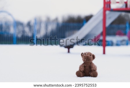 Lost teddy bear toy sitting on snow in winter,Lonely and sad brown bear doll sit alone in the in playground, Lost toy or Loneliness concept,International missing Children day