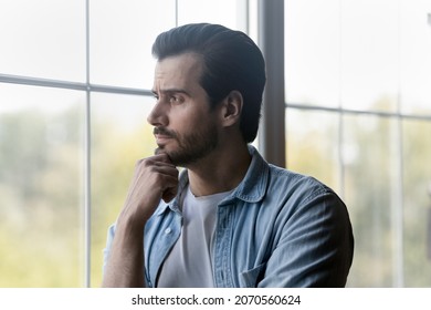 Lost In Thoughts. Pensive Millennial Bearded Guy Stand By Window Look At Distance Rub Chin Contemplate On Business Affair Ponder On Choice. Thoughtful Young Man Make Decision Think On Problem Solution