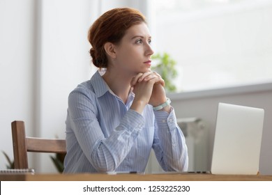 Lost In Thoughts Woman Sits At Workplace Desk In Office In Front Of Laptop Holds Hands On Chin Looking Away Thinking About Working Moments. Businesswoman Planning Or Trying Solve Some Business Issues