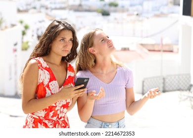 Lost tourists checking location on smart phone in a white town street on summer vacation - Shutterstock ID 2214672353