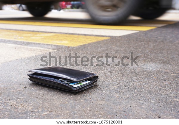 The\
lost wallet lies on the road near the crosswalk with a passing car\
in the background.                              \
