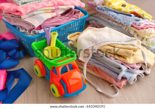 Lots of children\'s clothes. A lot of children\'s\
clothing piled on a wooden background. Clothes for babies made of\
soft fabric. Multicolored clothes for children are made in the\
laundry basket.