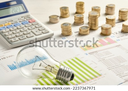 lots of coins a light bulb and a calculator on two electricity bills with graphs and consumption data
