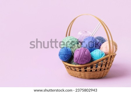 Lots of colorful knitting balls in a basket with knitting needles on a pastel purple background. Set for the hobby of knitting warm clothes or toys. Concept needlework