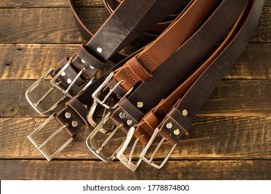 Lots of handmade men's leather belts on a wooden background. Classic men's leather belts in brown and cognac color. Handmade leather belts. Leather craft - Shutterstock ID 1778874800