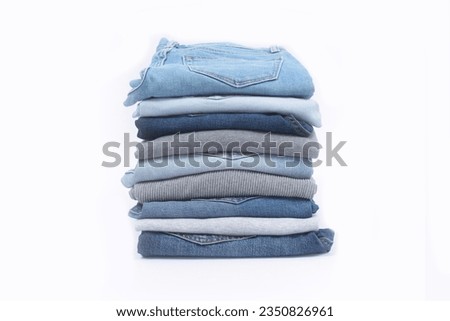 Lots of jeans pants with sweater in a stack. Denim background.