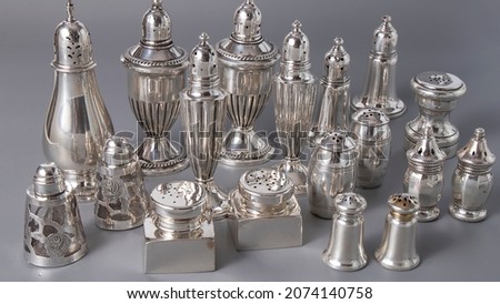 Lots of old silver salt shakers of different shapes  and sizes. Isolated shiny silverware on a gray surface.
