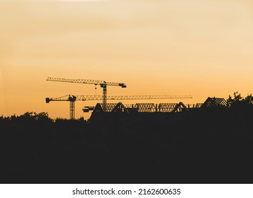 Lots of tower cranes build high-rise residential building in evening time. Steel frame structure in sunlight. Industrial background with sun flare. Yellow sunset sky.