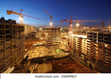 Lots Of Tower Cranes Build Large Residential Buildings At Night.