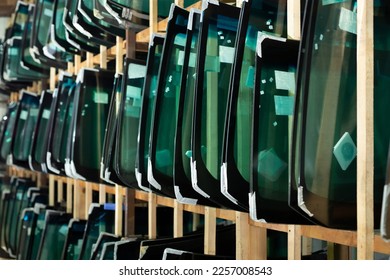 Lots of windshields for different cars on service station shelves ready to install or replace broken glass with cars. - Shutterstock ID 2257008543