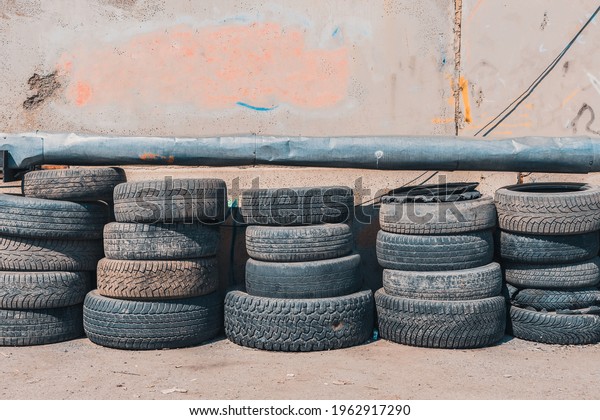 Lots of worn-out car tires stacked against a\
wall in a junkyard