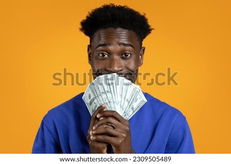 Lottery Luck. Happy African American young man has just won the lottery jackpot, holding bunch of cash dollar banknotes and smiling, isolated on yellow studio background, closeup