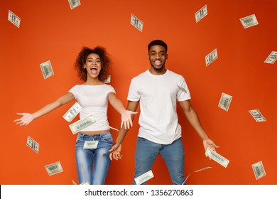 Lottery Winning. Emotional Rich African-american Couple Enjoying Money Banknotes Shower, Orange Background