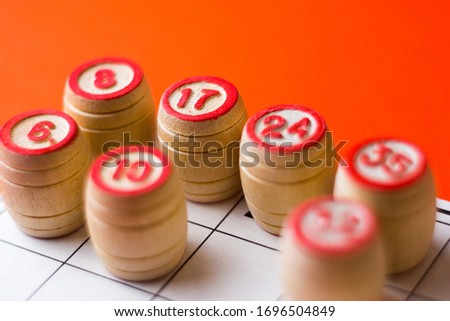 Lotto wooden barrels with numbers on a bright orange background. Some details are out of focus. Family bingo game. Conceptual photo.