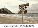 Loudspeakers or megaphones broadcasting a pole and a tsunami warning and evacuation sign located on the beach with old Jaffa in the background. Israel