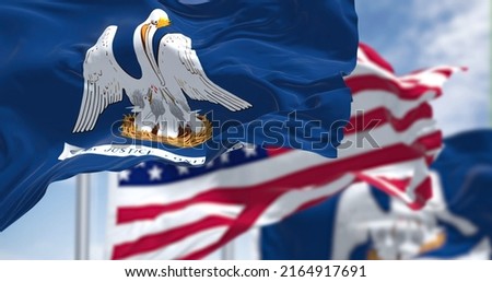 The Louisiana state flag waving along with the national flag of the United States of America. In the background there is a clear sky. Louisiana is a state in the Deep South regions of the US