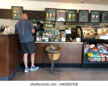 LOUISIANA, USA - JULY 26, 2019: A Caucasian Bald Man Wearing Workout Clothes And Nike Sneakers Buys Drink From Starbucks Coffee Shop. People Like To Drink Coffee In The Morning Before Going To Work.