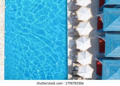 Lounge chairs with umbrellas near swimming pool on sunny day, top view