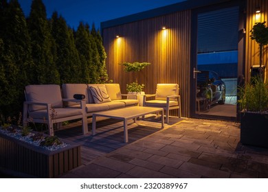 Lounge and Dining Area at Modern Residential Backyard Decorated with Outdoor Lights, Plants, Garden Table and Chairs. Cozy Summer Evening.